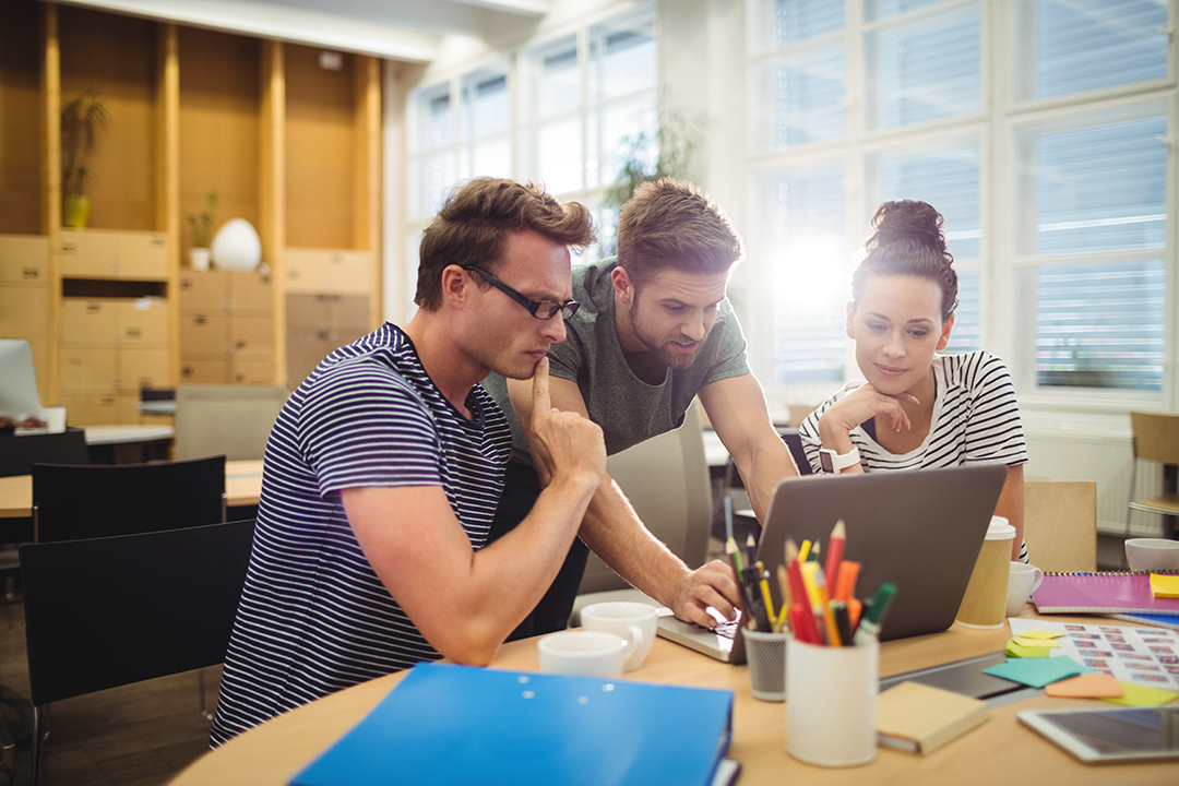 Group of graphic designers discussing over laptop at their desk in the office